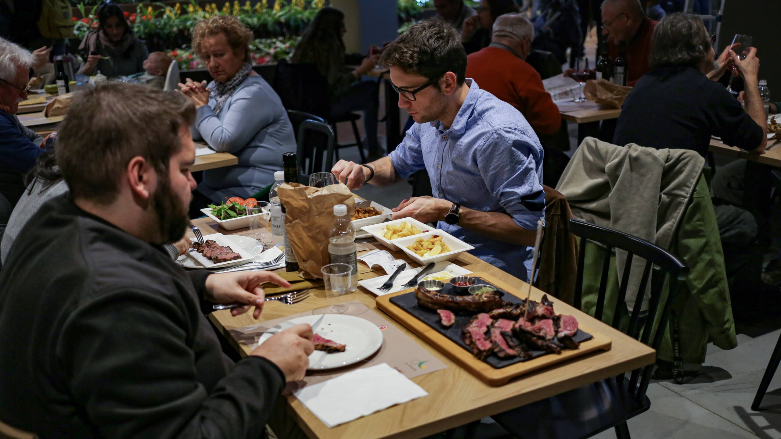 Sliced bistecca alla fiorentina on a slate board in a crowded Italian market hall