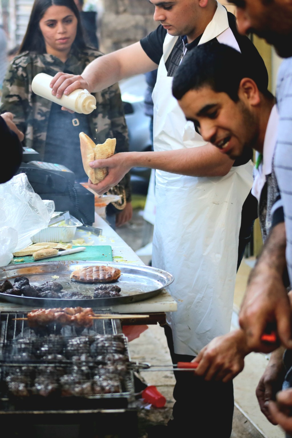 Street food vendors preparing pita sandwiches beside a charcoal grill